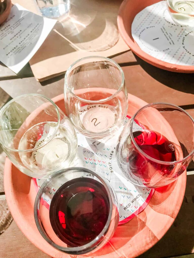 A close-up of a flight of four wine glasses, two containing white wine and two with red, sitting on a round tray with a wine-tasting card beneath each glass.
