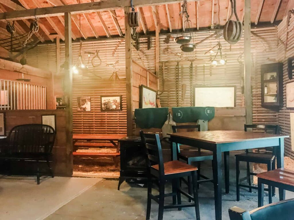 A rustic tasting room at McCall winery, housed in a repurposed barn with exposed wooden beams, historical horse tack hanging from the ceiling, and wooden tables set for guests.