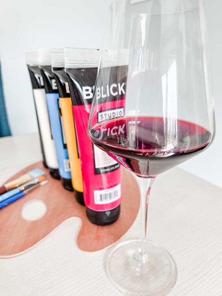 Glass of red wine and paint supplies