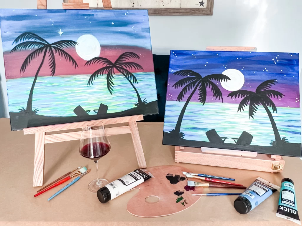 Two paintings of beach at night with glass of red wine