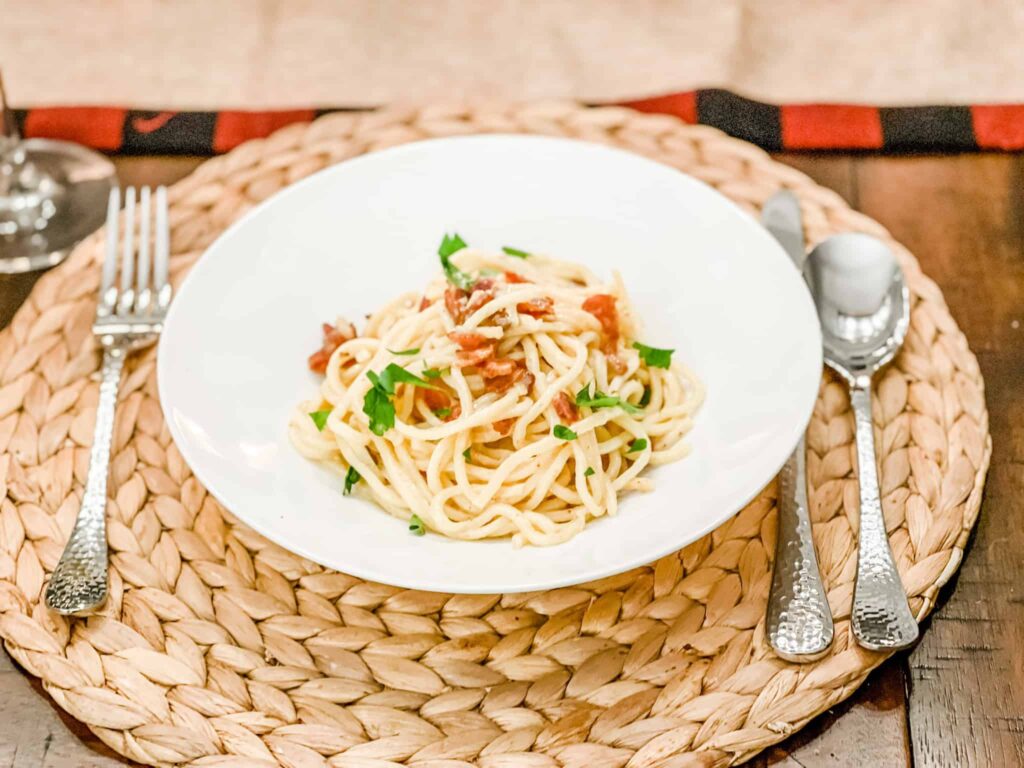 Spaghetti carbonara in a white bowl on a placemat set for dinner