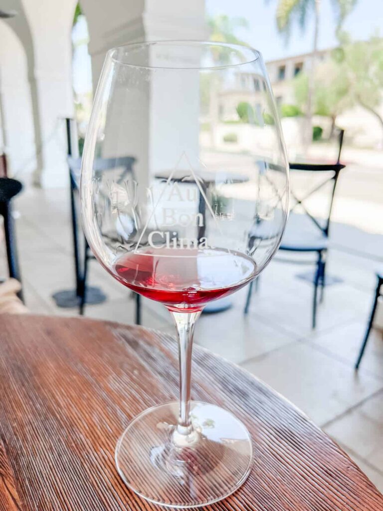 An elegant glass of red wine with a focused view on 'Au Bon Climat' etched onto the glass, showcasing the rich color of the wine, set on a wooden table with blurred patio background.