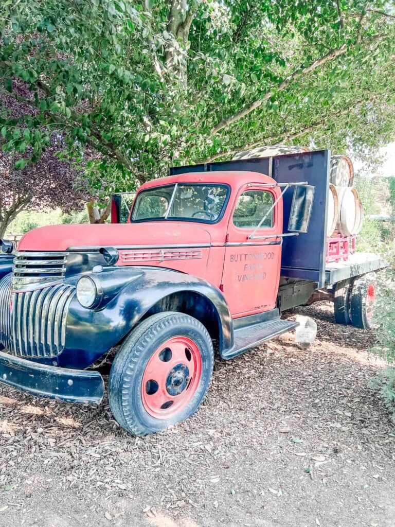 Vintage red Buttonwood Farm Winery truck with barrels in the back, parked under the shade of a tree.