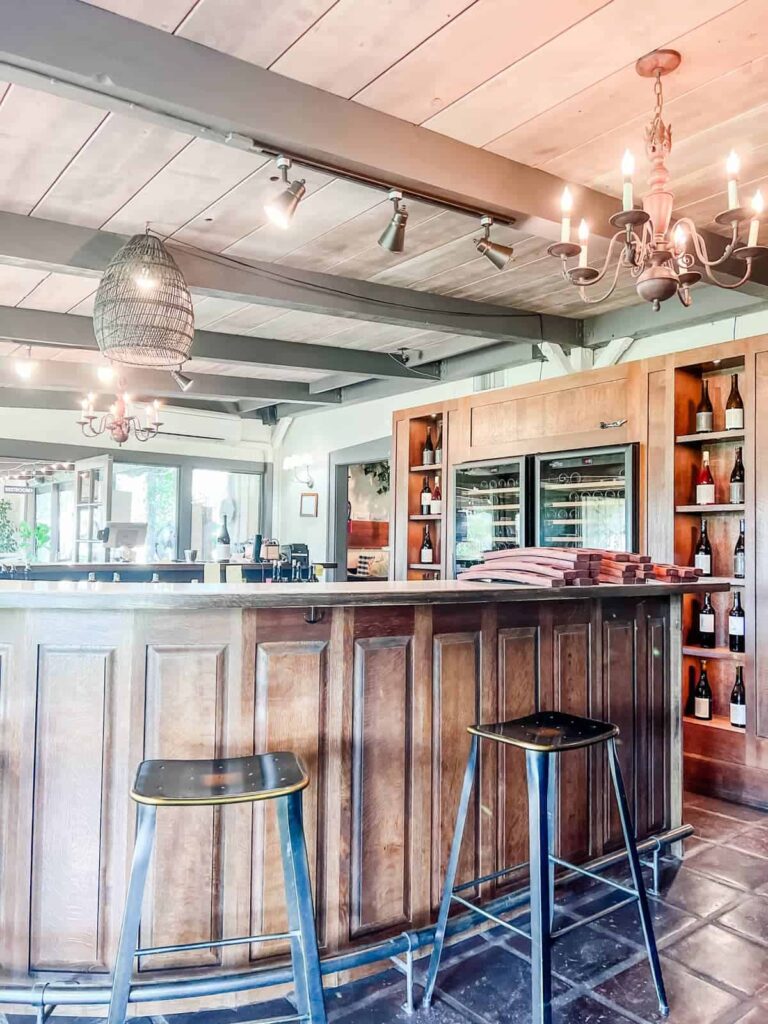 Wooden bar area inside Rideau wine tasting room with metal stools, a chandelier, and shelves displaying wine bottles.