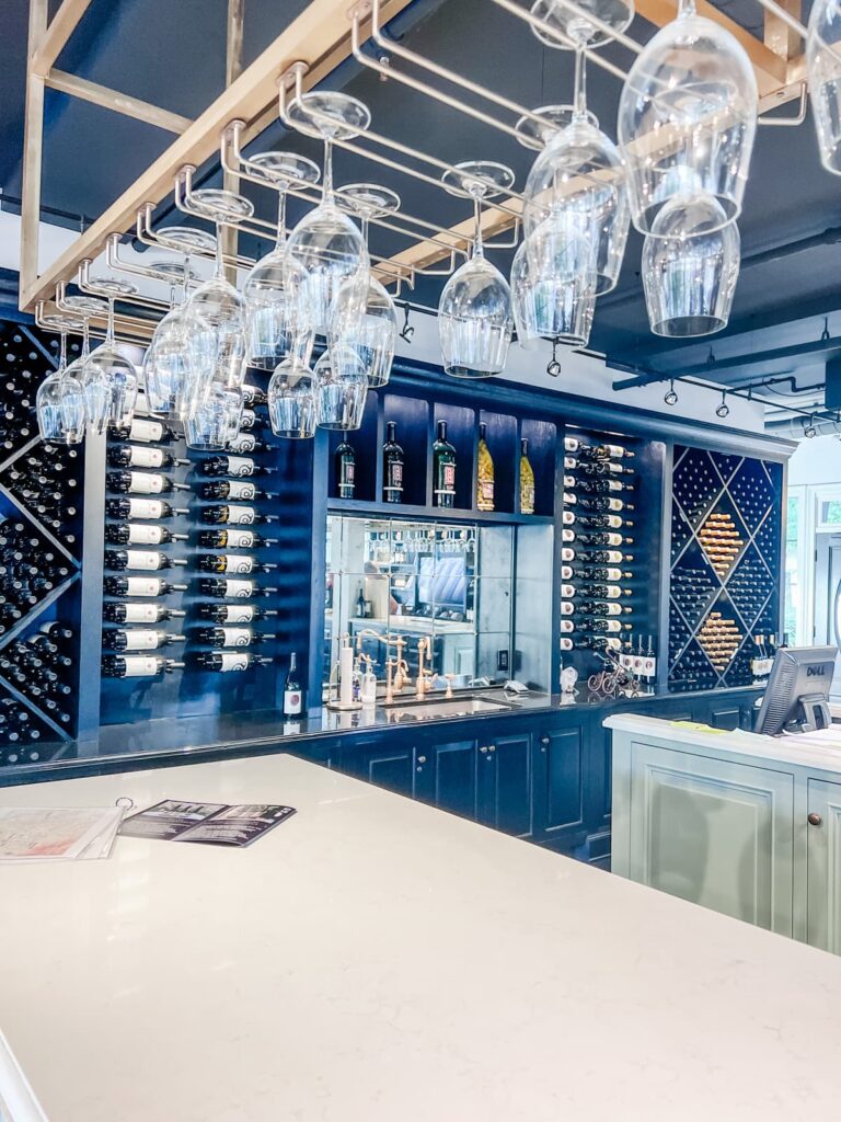 Sleek interior of Sanger Family wine bar with hanging wine glasses, a display of wine bottles, and a navy blue bar.