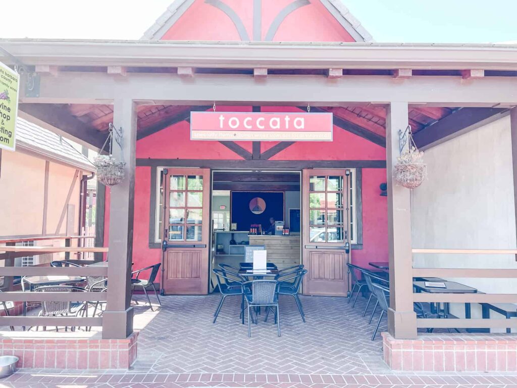 The welcoming entrance to Toccata tasting room, showcasing outdoor seating and the vibrant red exterior with hanging plants.