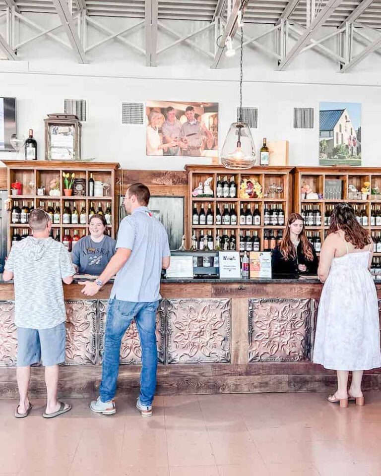Visitors engaging with staff at a rustic wine tasting bar, decorated with wooden accents and vintage elements inside a winery.