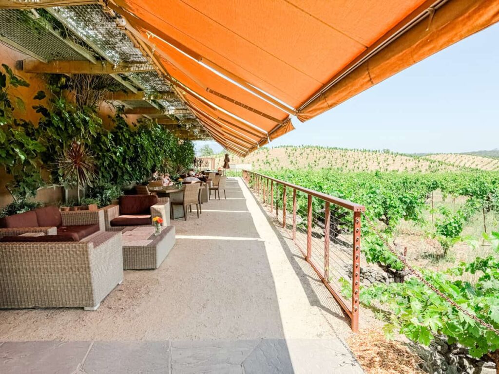 Shaded outdoor seating area at Ridge Vineyards Lytton Springs, with wicker furniture and views of surrounding vineyards under an orange awning.