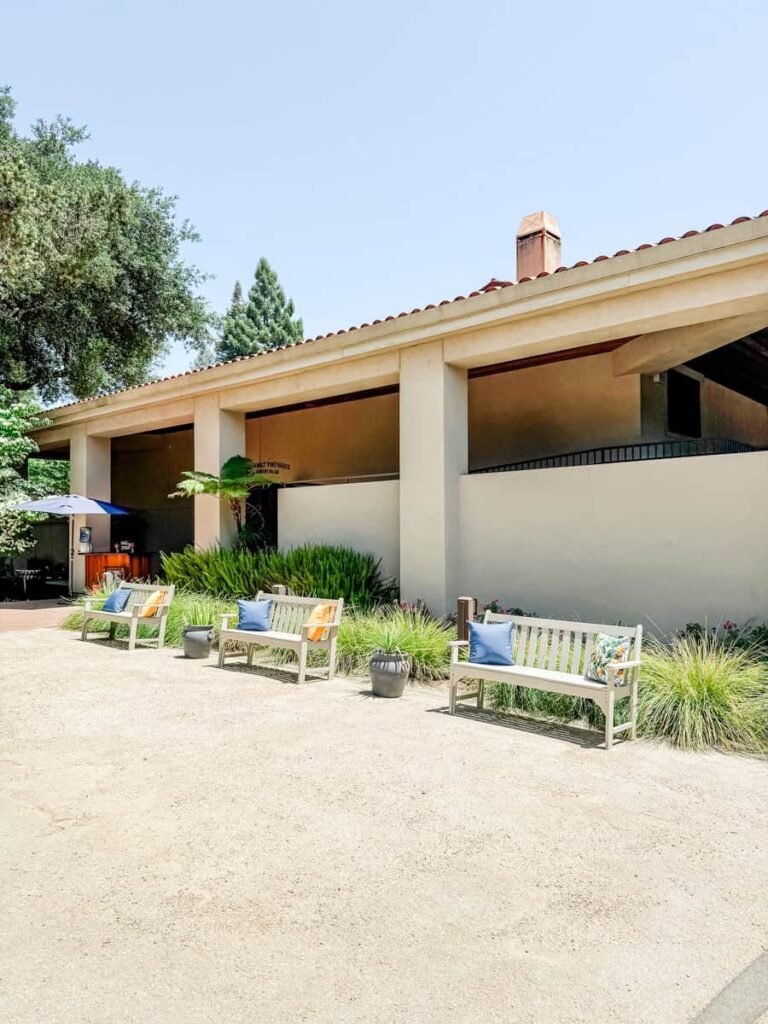 Exterior view of the Seghesio Family Vineyards tasting room, featuring white benches with colorful pillows and landscaping with ornamental grasses.