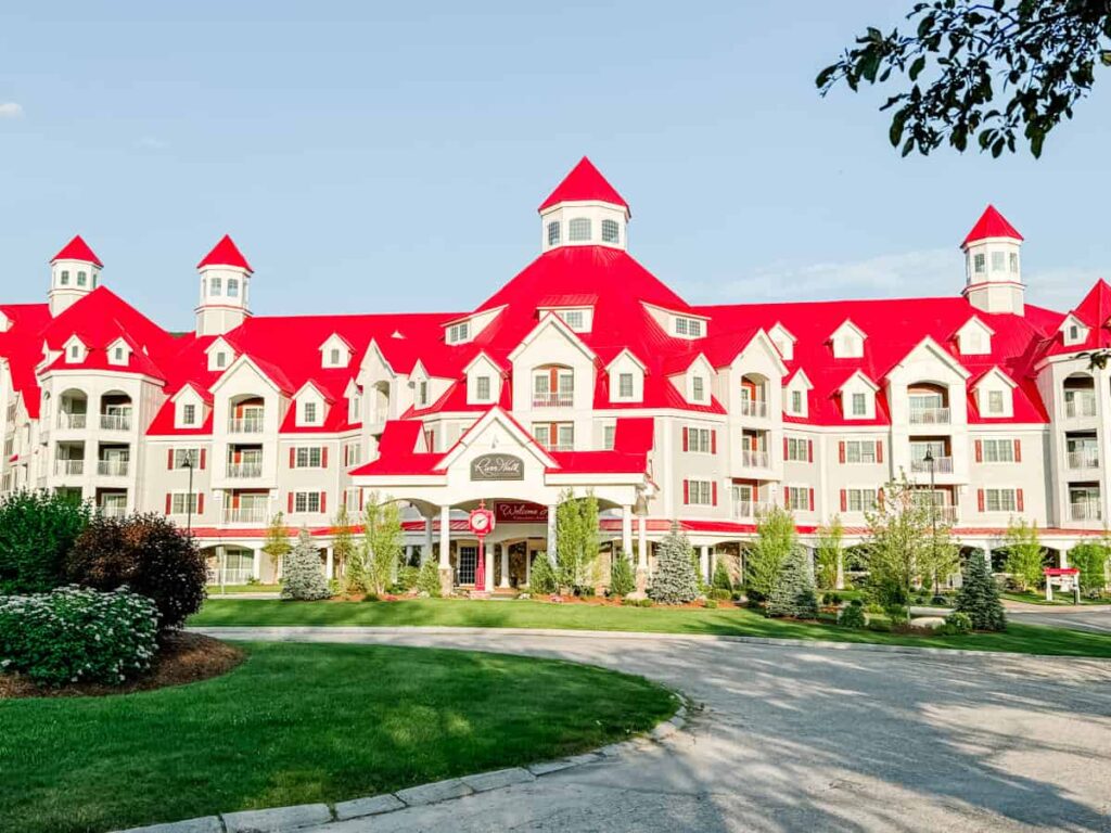 Grand Victorian-style resort building with bright red roofs and white trim, home to Seven Birches Winery in Lincoln, New Hampshire, surrounded by neatly landscaped lawns and evergreens.