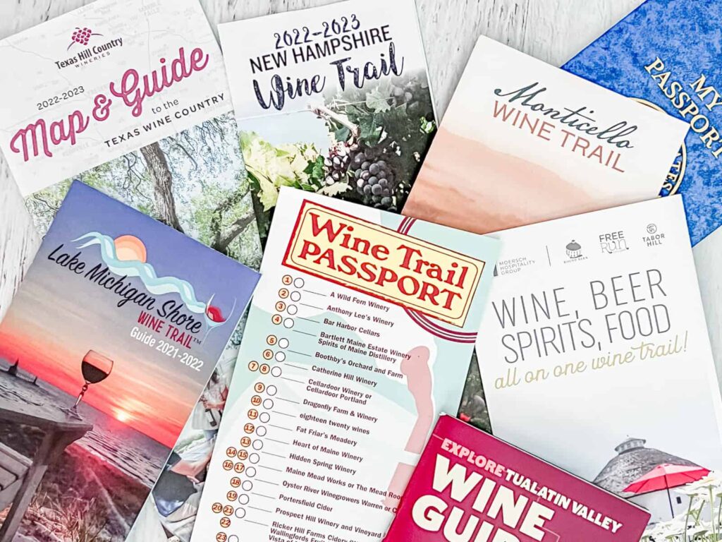 An assortment of wine passports and guides laid out, featuring the Texas Wine Country Map & Guide, Monticello Wine Trail, Lake Michigan Shore Wine Trail Guide, and a Maine Wine Trail Passport with a checklist of wineries.