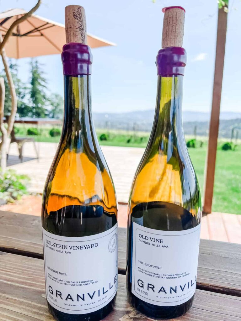 Two bottles of Granville Wine Co. Pinot Noir on a wooden table, labeled "Holstein Vineyard 2021 Pinot Noir" and "Old Vine 2022 Pinot Noir."