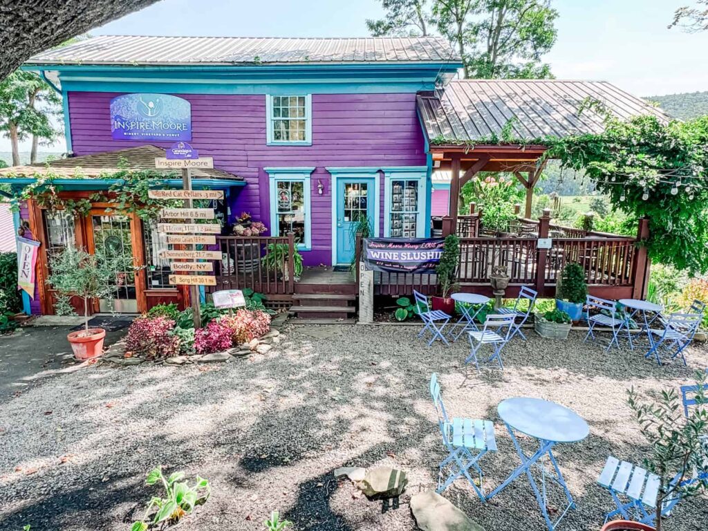 A vibrant purple-painted building with turquoise accents, surrounded by a charming gravel patio with blue outdoor seating, adorned with colorful flowers and
