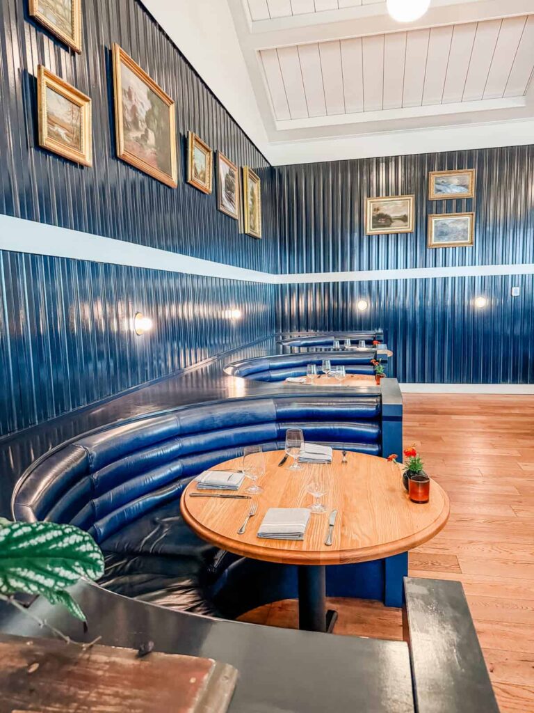 A corner seating area at Rose Tavern with curved leather banquettes, round wooden tables, and framed paintings on dark wooden panel walls.