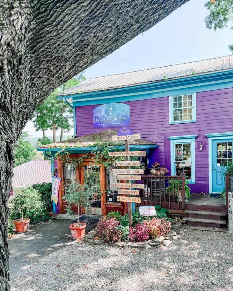 The vibrant purple-painted Inspire Moore tasting room building with turquoise accents, adorned with colorful flowers.