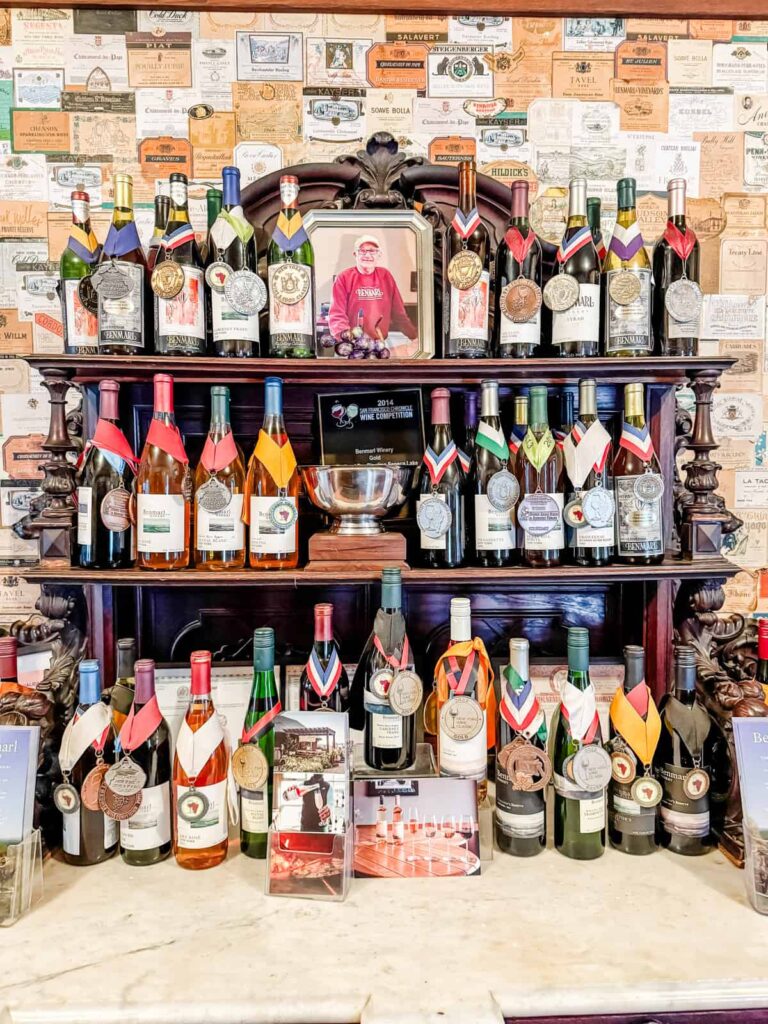 A collection of award-winning wines displayed on an antique wooden shelf, with medals and ribbons adorning the bottles, against a backdrop of vintage wine labels.