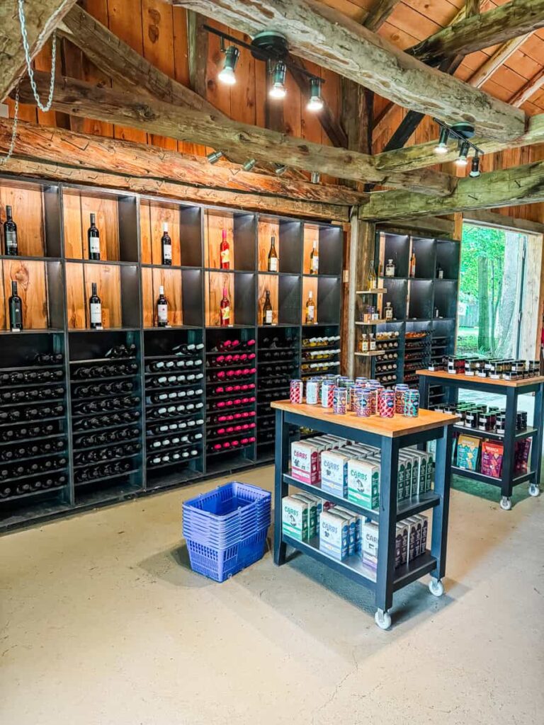 Inside Domaine du Ridge's boutique, featuring shelves lined with bottles of wine, cider cans, and local products beneath exposed wooden beams.