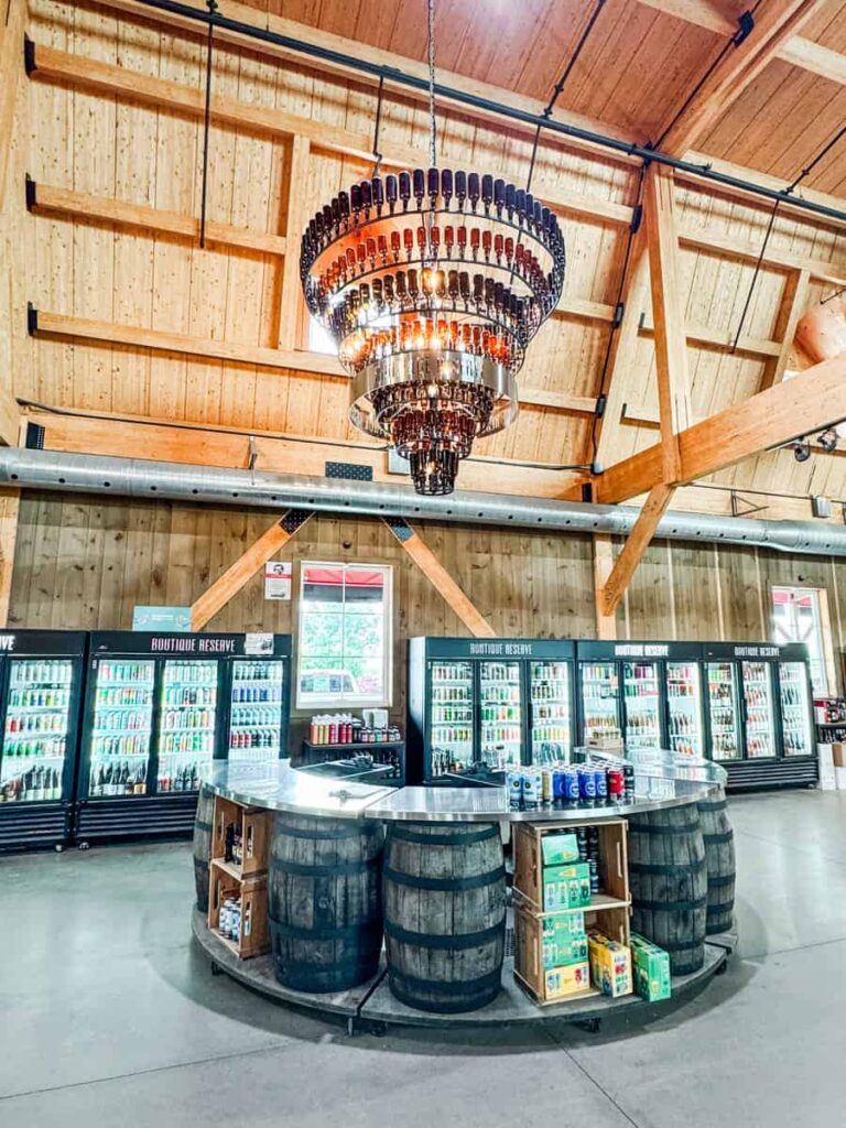 Wide view of Ferme Guyon's boutique with wooden beams, a chandelier made of glass bottles, and coolers stocked with local beverages.