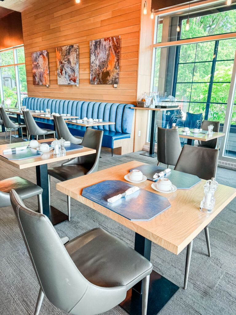 Bright, stylish dining area at La Cache du Lac Champlain with modern tables, leather chairs, blue banquette seating, and large windows letting in natural light.