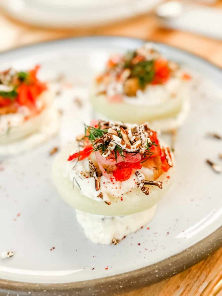 Close-up of the Première Entrée at Les Cocagnes, featuring kohlrabi rounds topped with house kimchi, crispy puffed rice, herbs, and marinated shallots.