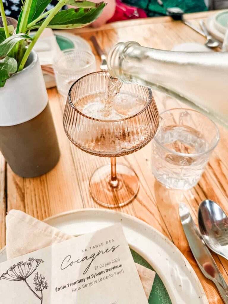 Rosé being poured into a faceted coupe glass at a set table, with a menu card for La Table des Cocagnes.