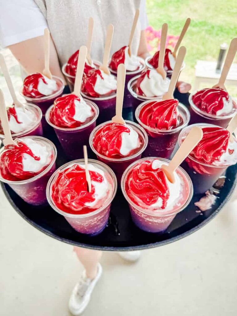 A server holding a tray of frozen black currant treats from Cassis Monna & Filles, served in clear cups with wooden spoons.