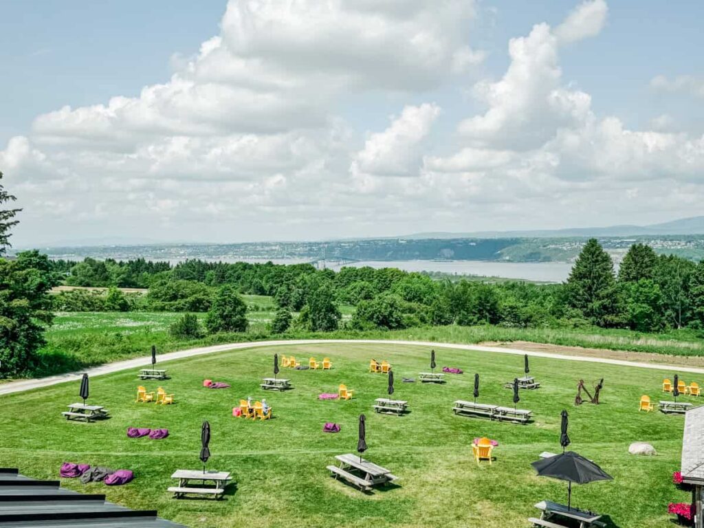 The expansive lawn at Cassis Monna & Filles with picnic tables, Adirondack chairs, and sweeping views of the St. Lawrence River and surrounding greenery.