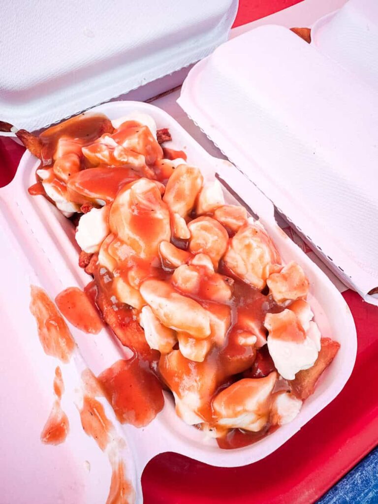 A classic Quebec poutine from Chez Mag, featuring fries topped with cheese curds and rich brown gravy, served in a compostable takeout box.