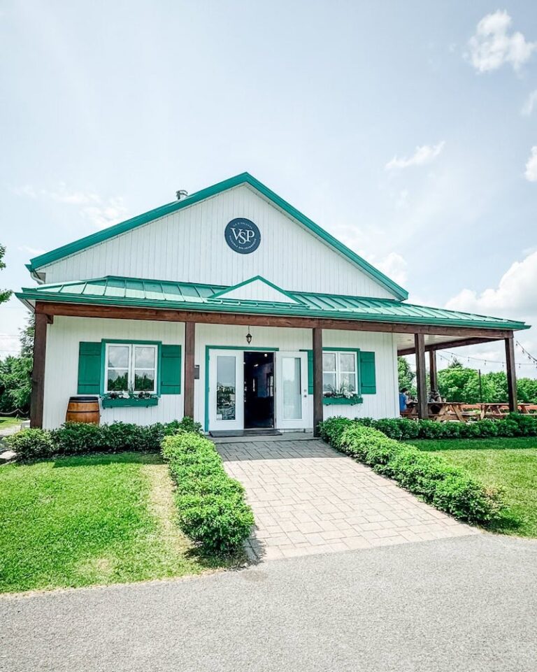 The charming tasting room at Vignoble Ste-Pétronille, featuring green shutters, a green metal roof, and manicured hedges lining the walkway.