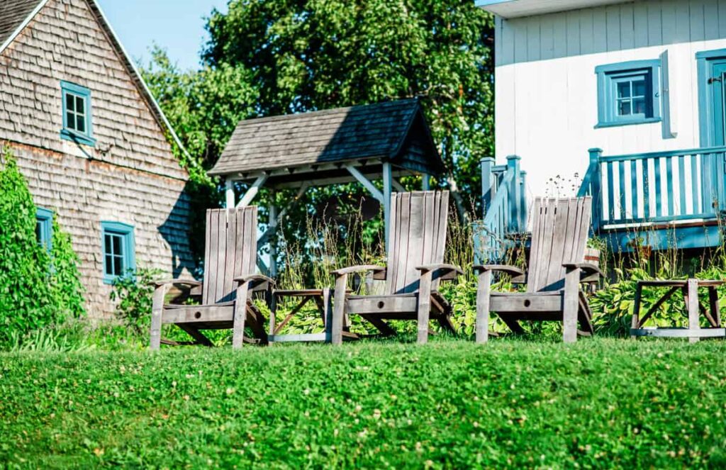 Three rustic Adirondack chairs sit on a grassy hill surrounded by charming buildings at Vignoble de l’Isle de Bacchus.