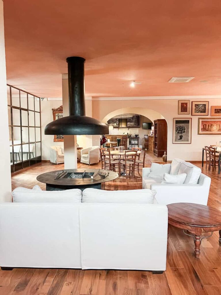 Cozy interior of Castello Monterinaldi lounge with white sofas, wooden floors, a modern black fireplace, and decorated walls, creating an inviting space for wine lovers and travelers.