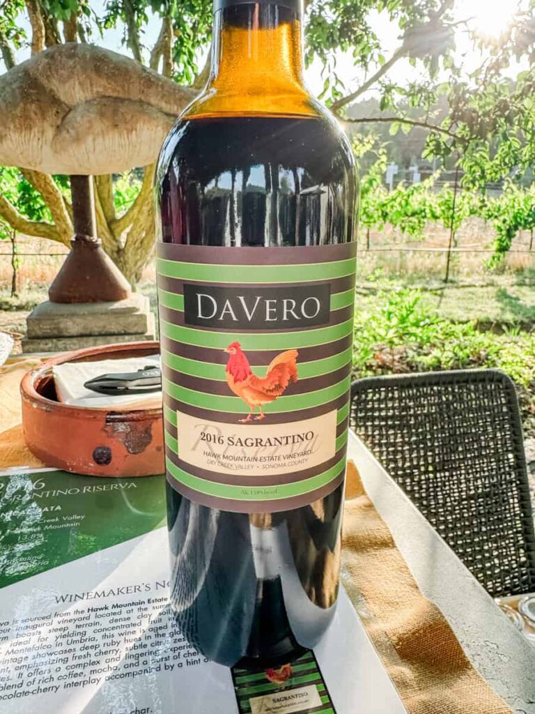 A bottle of DaVero 2016 Sagrantino wine from the Hawk Mountain Estate Vineyard in Dry Creek Valley, placed on an outdoor table with vineyard views in the background.