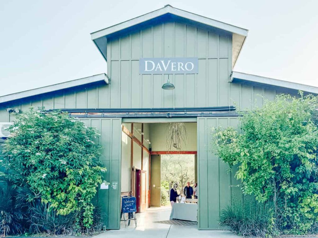 The exterior of DaVero Farms & Winery, featuring a sage green barn-style building with open double doors welcoming guests inside.