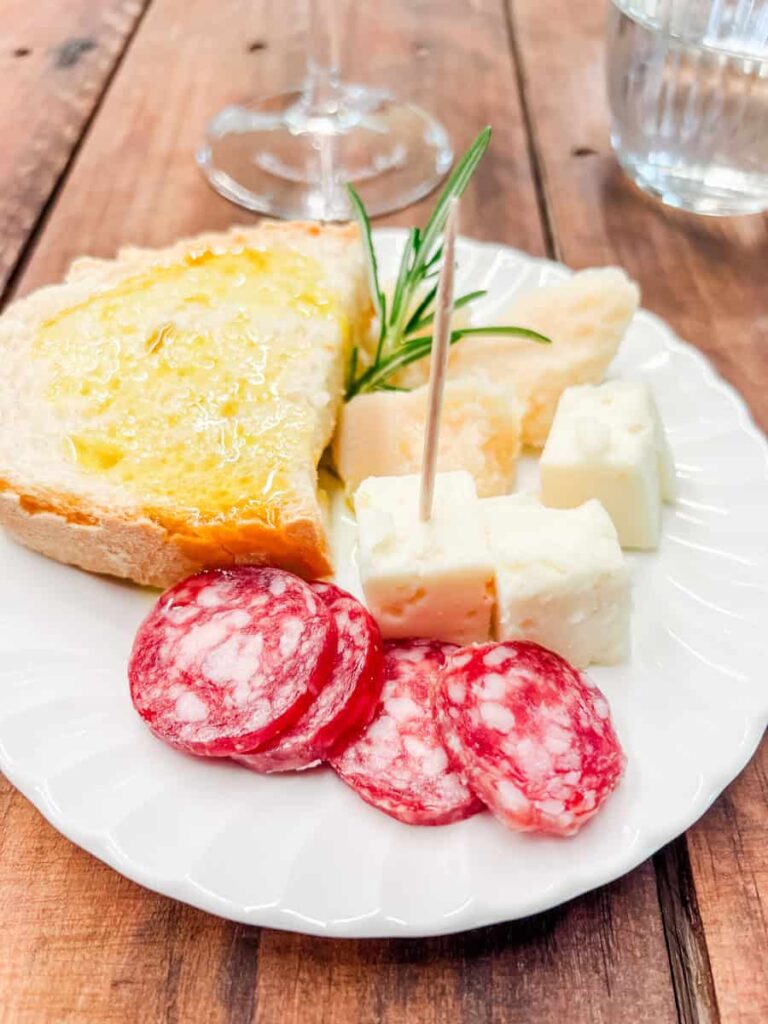 Cheese and charcuterie plate at Fattoria di Montemaggio featuring slices of cheese, salami, and bread, garnished with a sprig of rosemary on a white plate.
