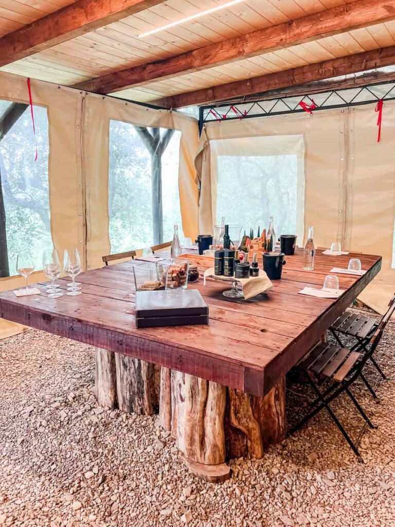 Rustic outdoor wine tasting table set up inside a beige tent with a wooden roof at Fattoria di Montemaggio.