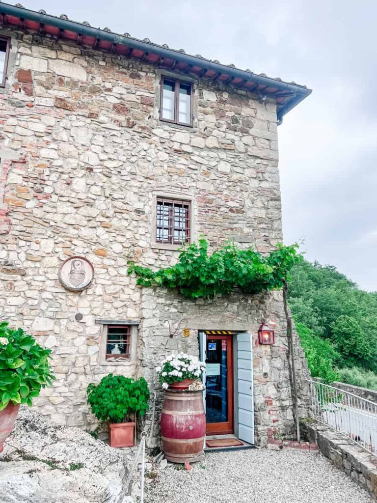 Il Barlettaio's rustic stone building with grapevines, potted plants, and vintage wine barrel outside in the Tuscan countryside.