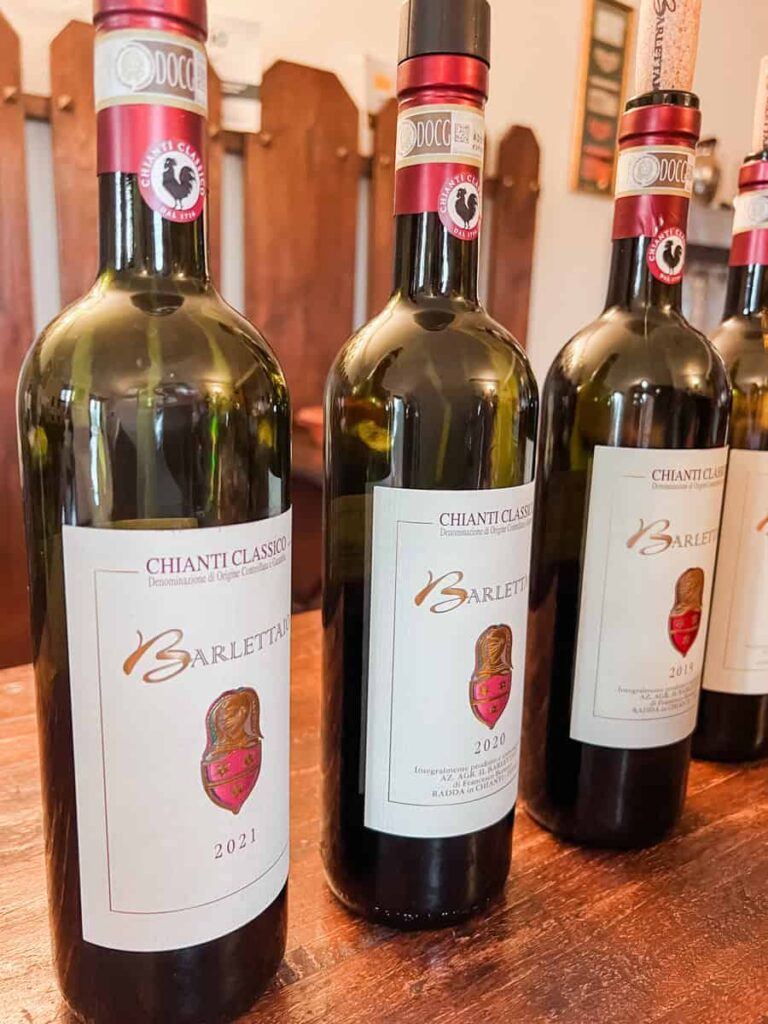 Bottles of Il Barlettaio Chianti Classico wine with a red and gold label featuring a coat of arms, displayed on a wooden surface in a wine shop.