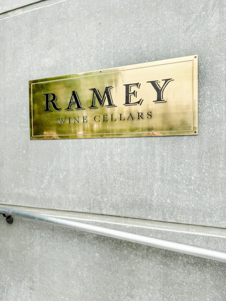 Gold Ramey Wine Cellars sign on a textured wall with a metal handrail below.