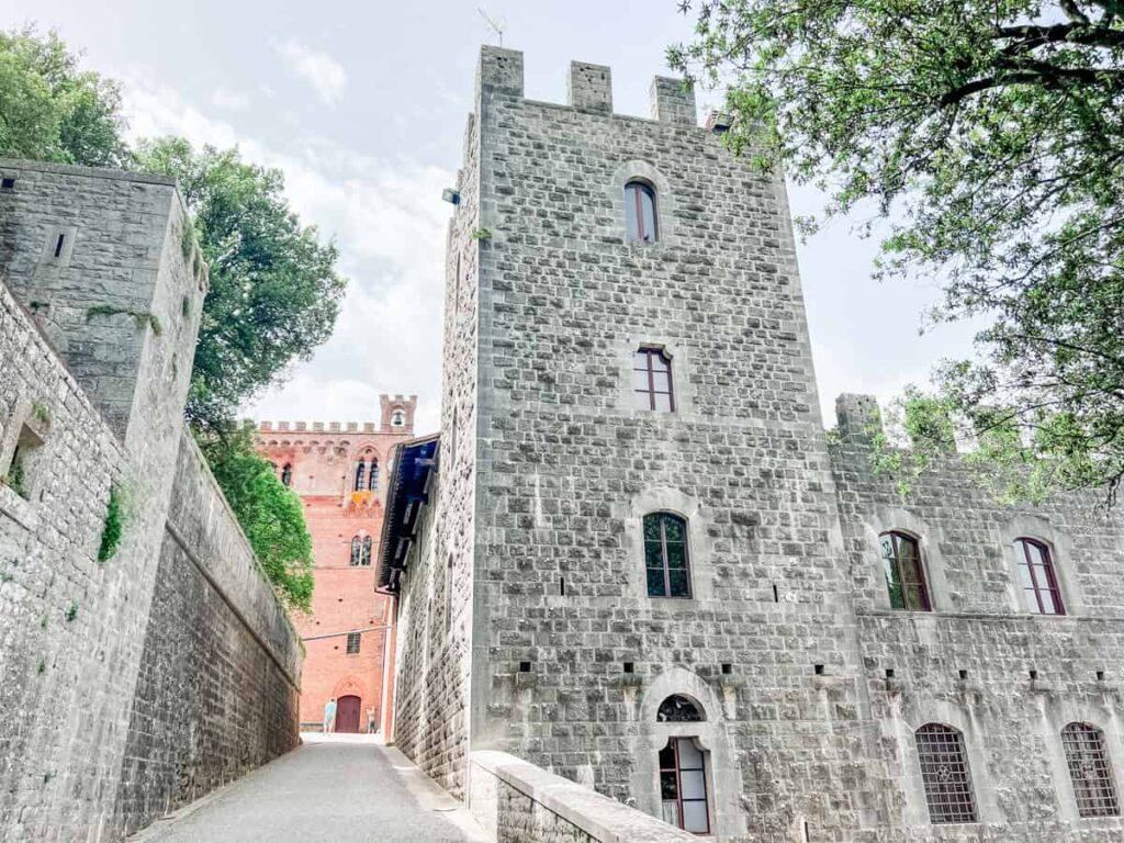 Ancient stone castle with tall towers and small arched windows, surrounded by green trees on a partially cloudy day.