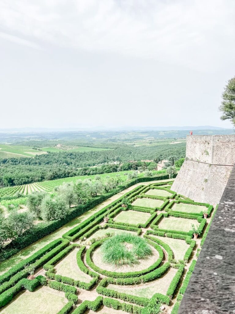 Vineyard garden with geometric hedges and a scenic view of rolling green hills in the background, overlooking the countryside from an ancient stone fortress wall.