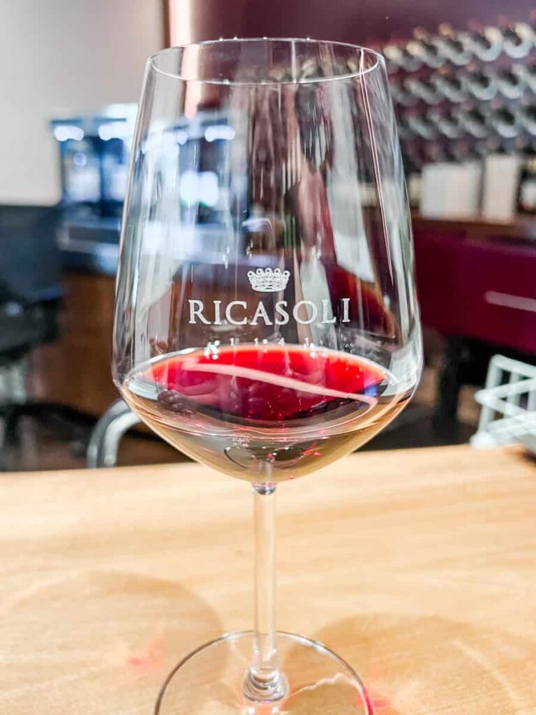 A glass of red wine with "Ricasoli" engraved on it, placed on a wooden table in a wine bar setting.