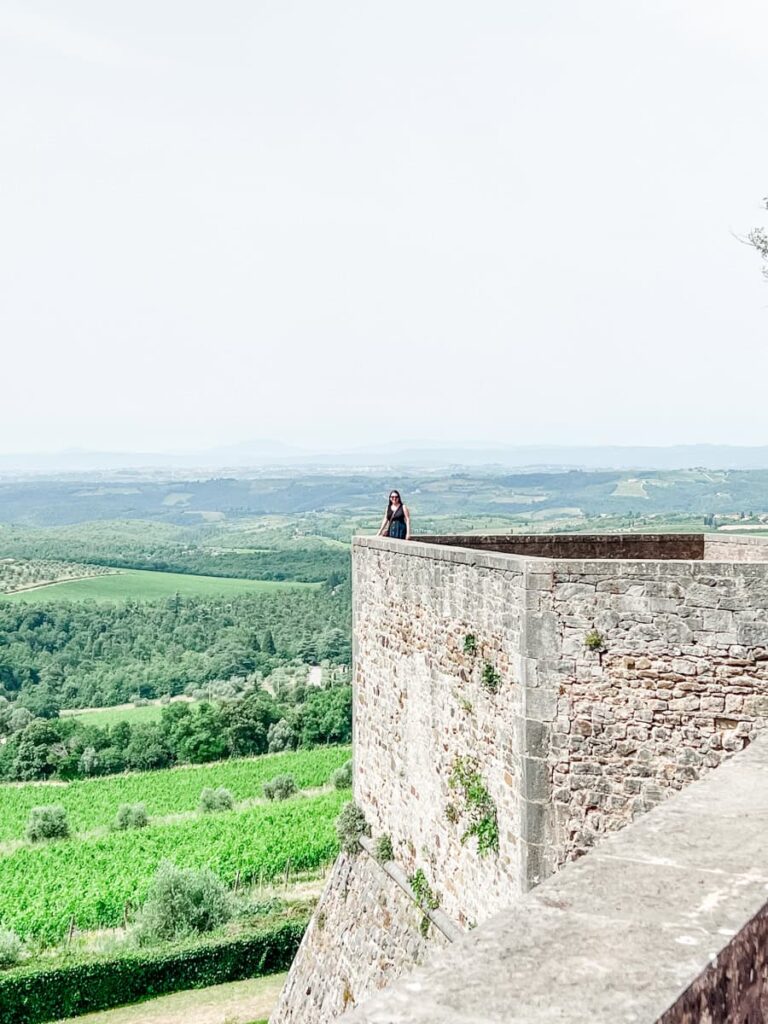 Laura of Wine Travelista standing on a stone terrace overlooking lush green vineyards and countryside under a cloudy sky.