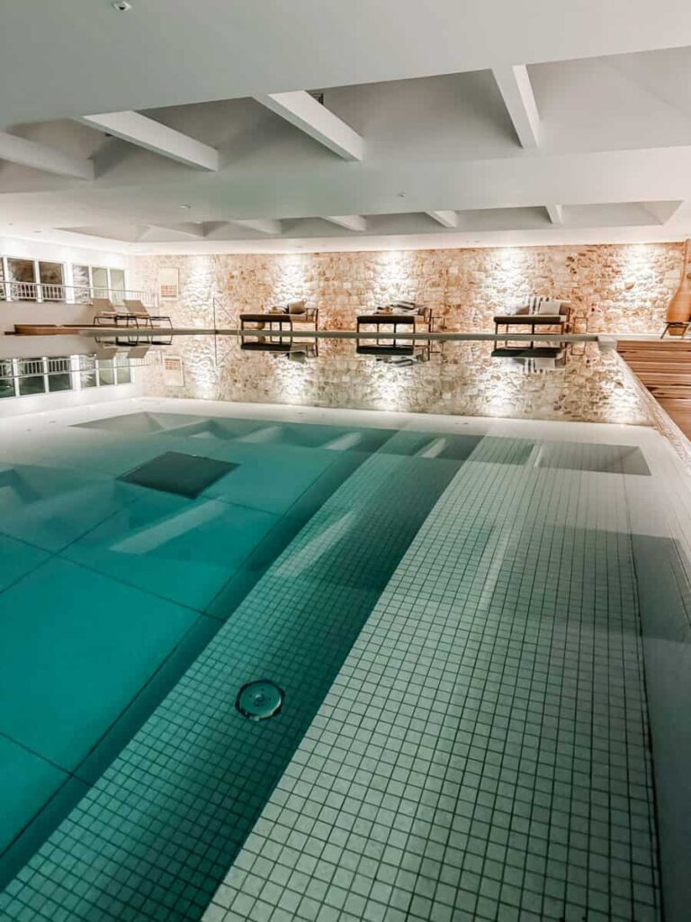 Indoor spa pool at Adriana Spa Hotel in Hvar Town, with sleek tilework, ambient lighting, and cushioned lounge beds along a stone accent wall.