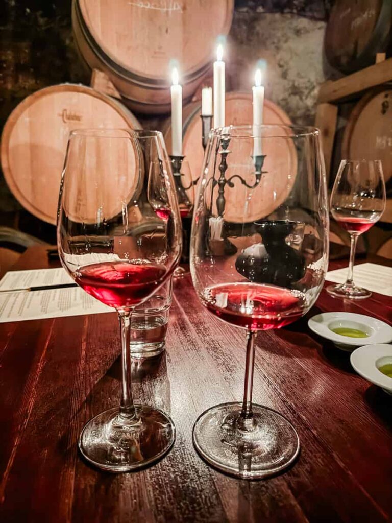 Close-up of red wine glasses during a tasting at Duboković Wines, with flickering candlelight and barrels in the background.