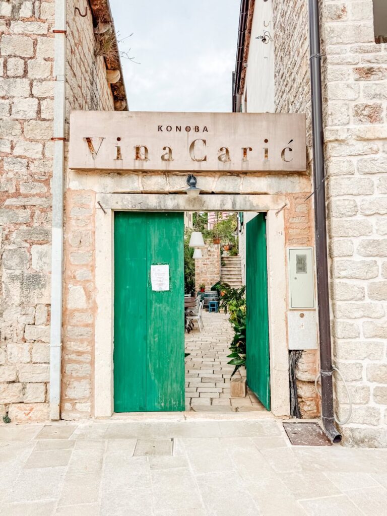 Stone entrance to Vina Carić in Hvar, Croatia, with green double doors leading into the winery's inviting courtyard.