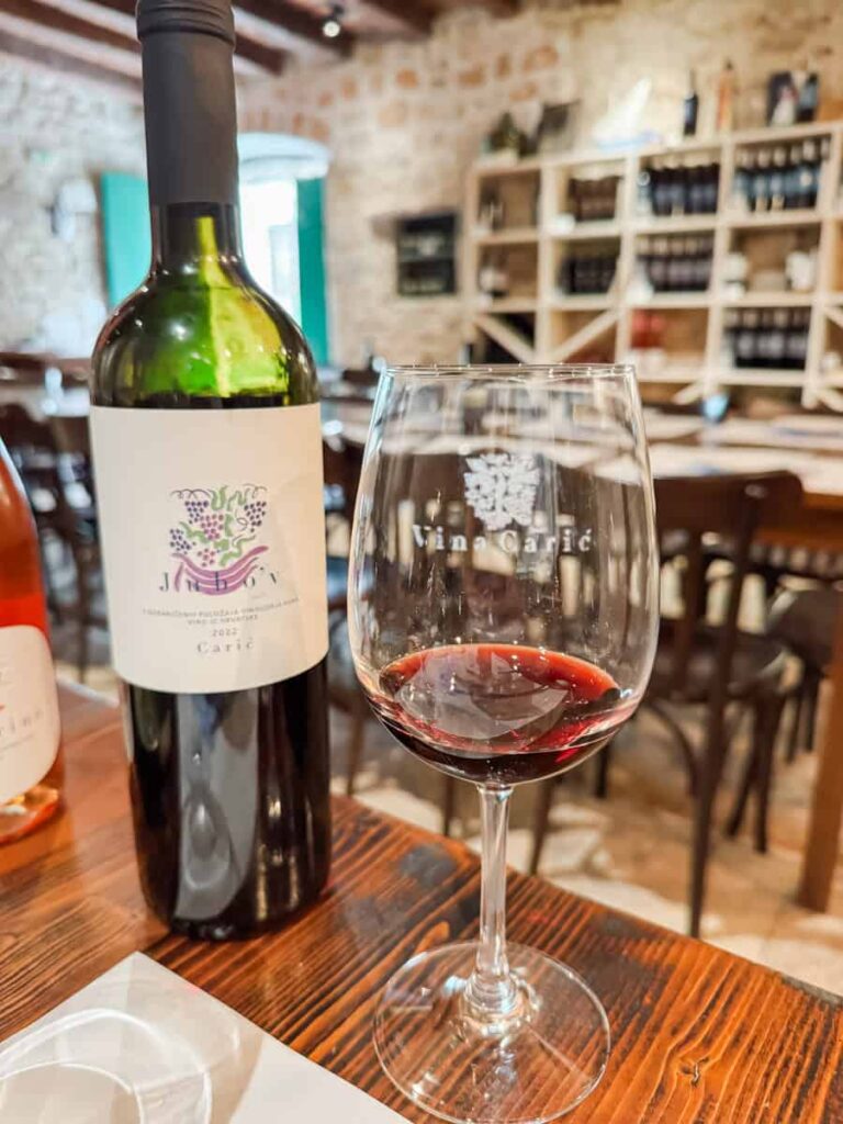 Glass of red wine and a bottle of Vina Carić’s 2022 Jubo’v blend set on a tasting table inside the winery.