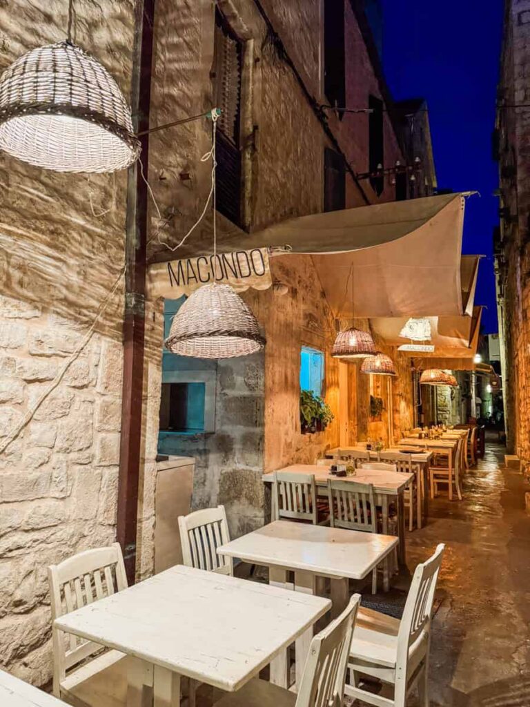 Narrow stone alley lit by warm lanterns with white wooden tables outside Macondo restaurant in Hvar.
