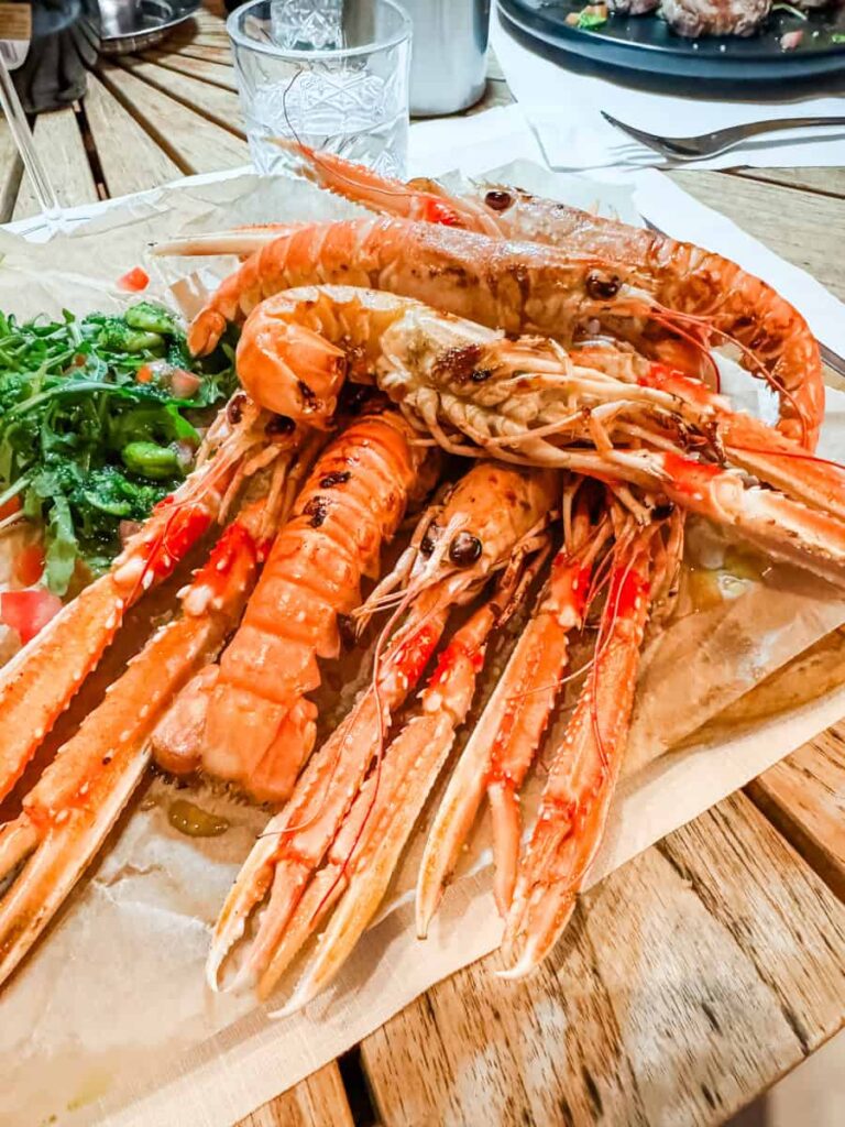 Generous serving of grilled scampi on a wooden plate, accompanied by a side of arugula.