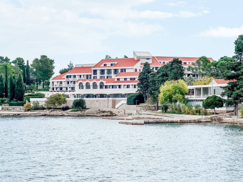 Aminess Liburna waterfront hotel on Korčula Island with red-tiled roofs, terraces, and trees along the Adriatic shoreline.