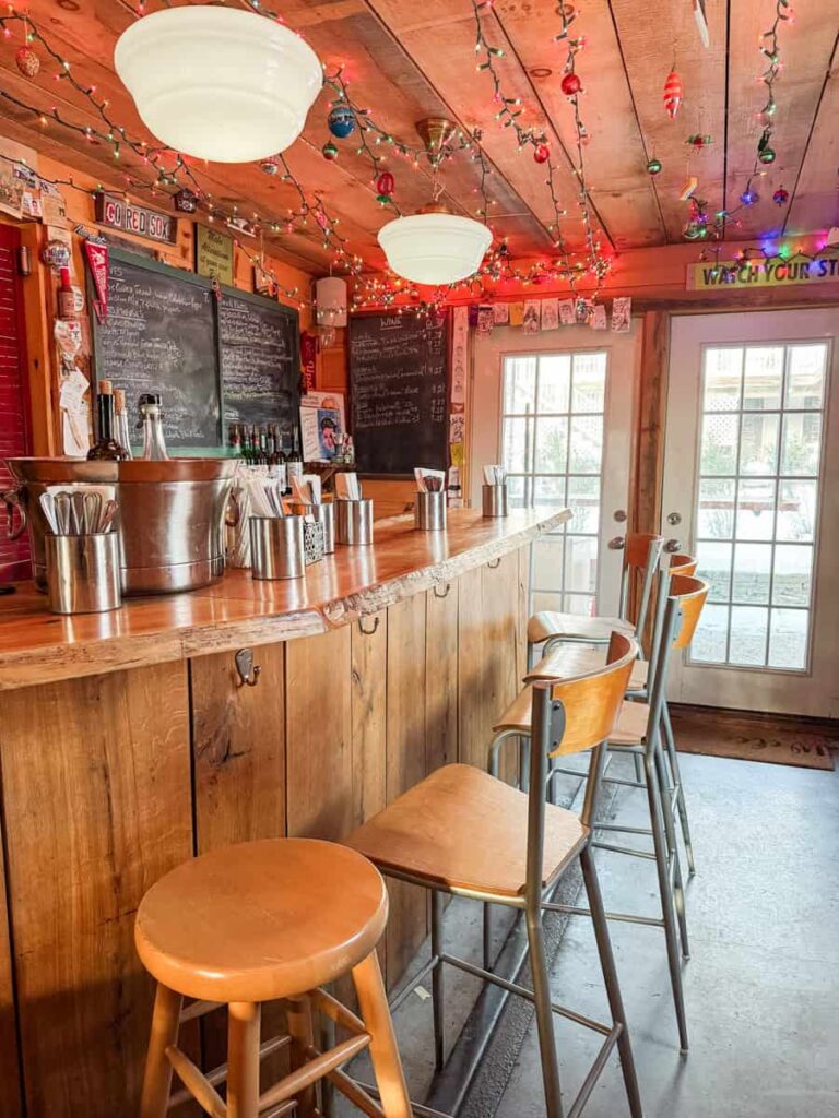 Cozy interior of Callicoon Wine Merchant featuring a wooden bar, chalkboard menus, and festive string lights hanging from the ceiling.